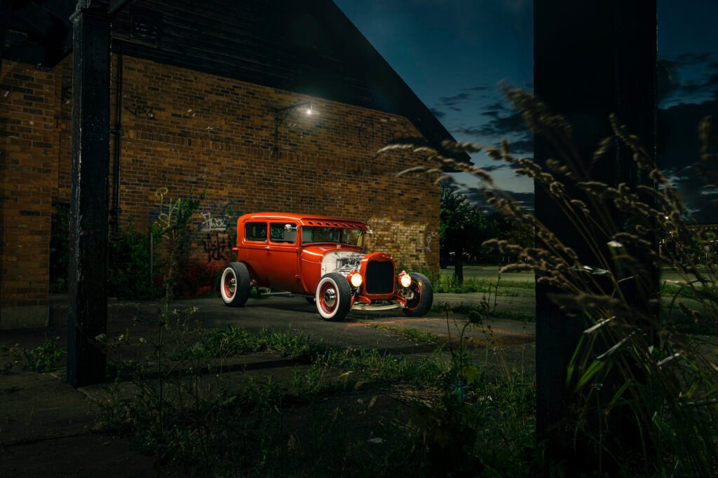 Red 1928 Ford Model A hot rod parked beside a brick warehouse at night