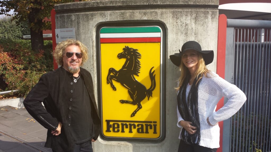 Sammy Hagar standing beside Ferrari sign at factory.