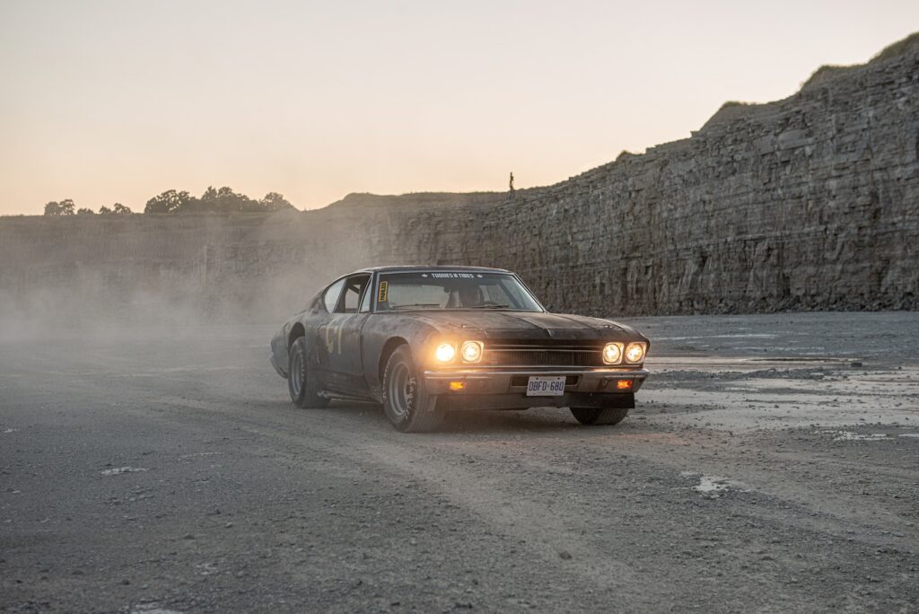1968 Chevrolet Chevelle driving with headlights on at dusk in quarry
