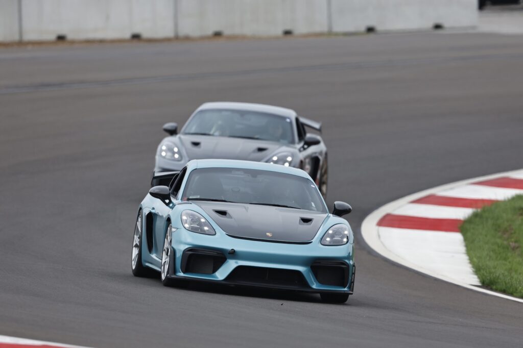 Light blue Porsche sports car leading another performance car through a racetrack corner