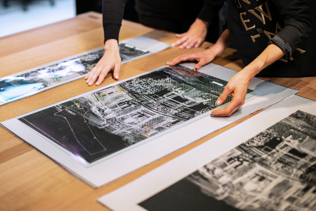 Hands arranging layered couture fabric panels featuring architectural illustrations