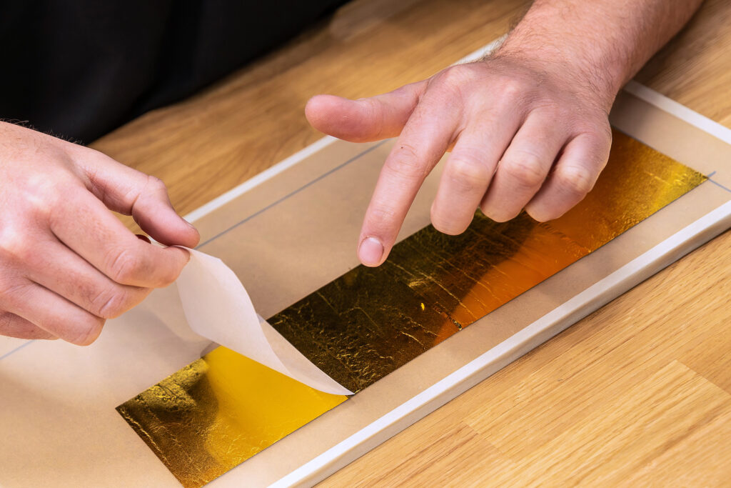Gold leaf squares aligned on a panel during precision gilding work