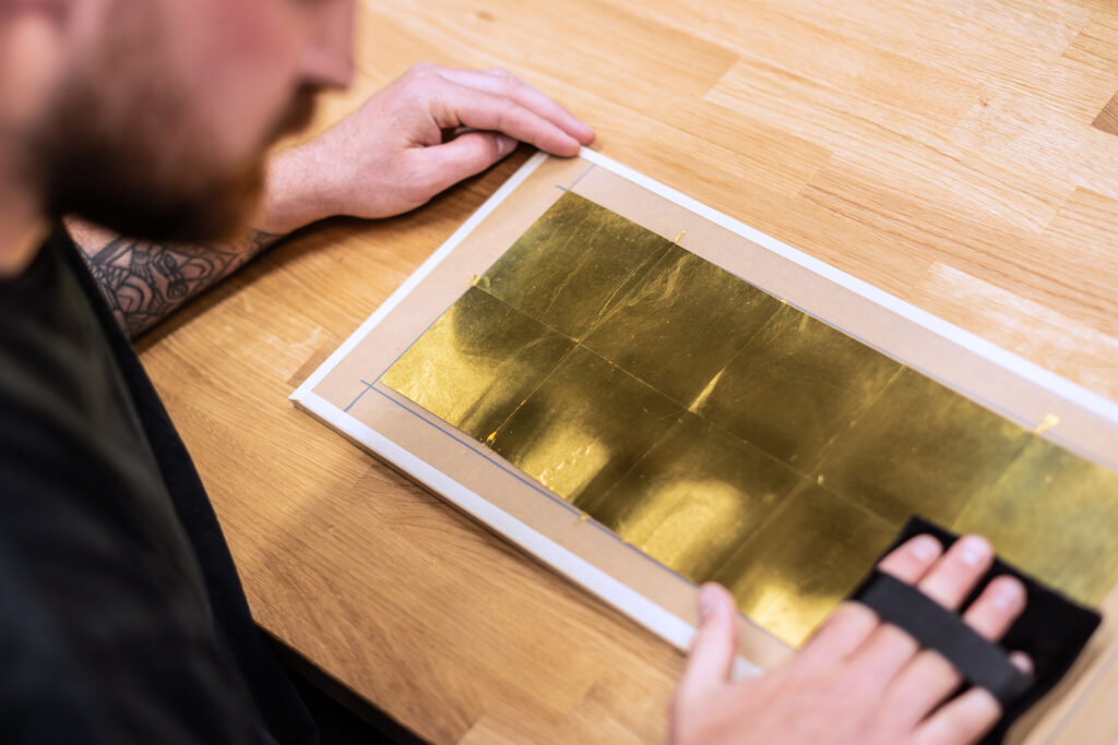 Craftsperson smoothing gold leaf onto a flat surface using traditional technique