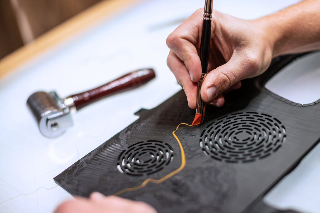 Artisan using a specialised tool to refine gold inlay on a wood panel
