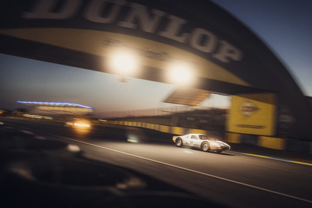 Classic Porsche 904 race car driving under illuminated Dunlop Bridge at night during Le Mans Classic