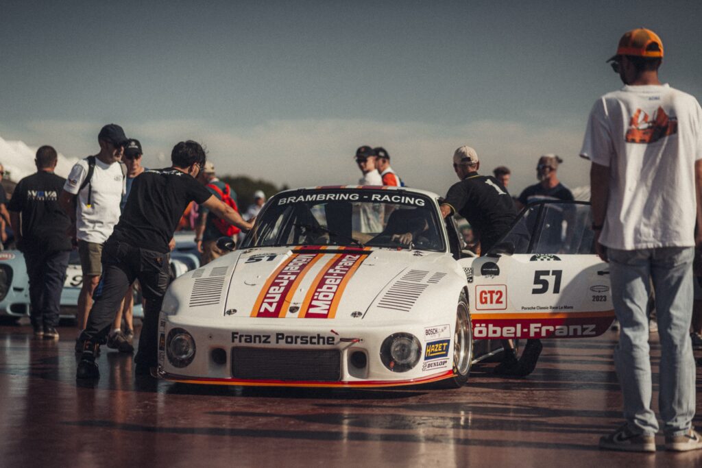 Crowd gathered around a classic race car on the grid at Peter Auto Classic Le Mans