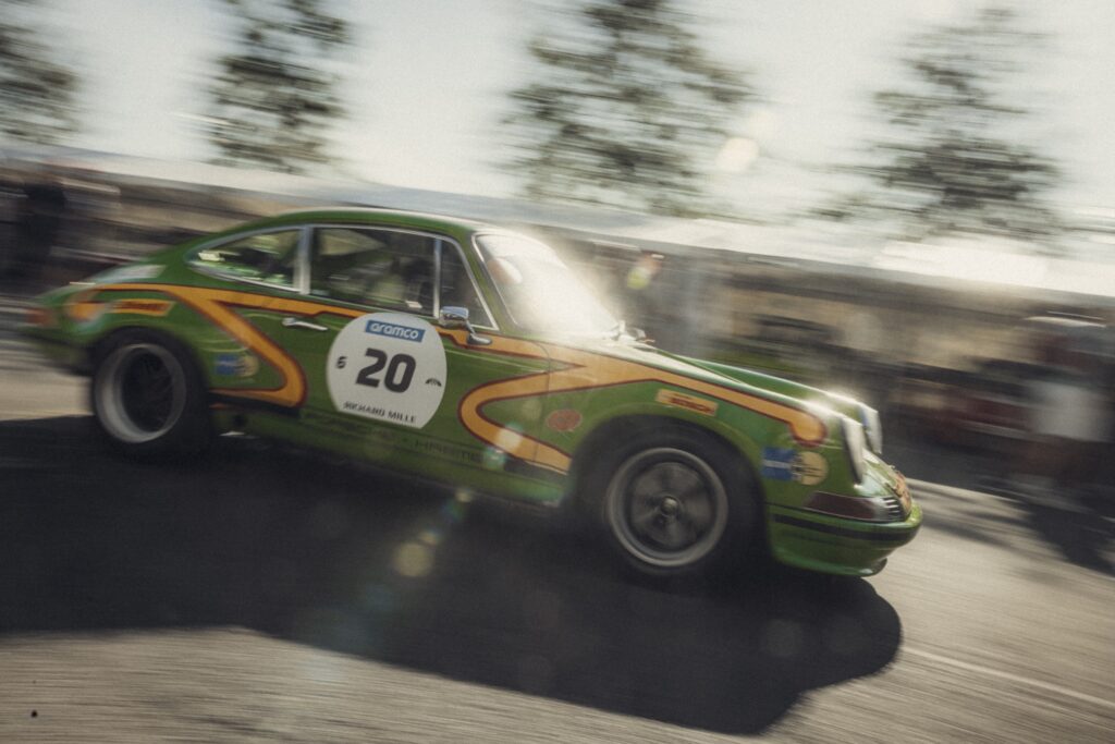 Green vintage Porsche 911 racing past in a motion-blur trackside scene