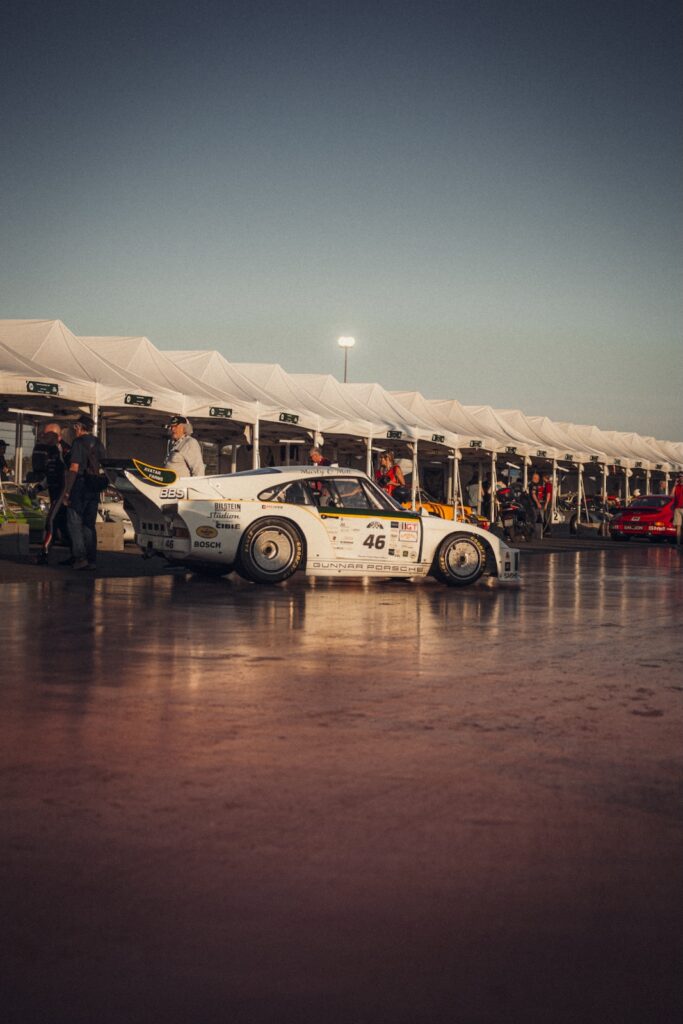White Gunnar Porsche 935 race car parked in paddock beside row of white team tents at Le Mans Classic