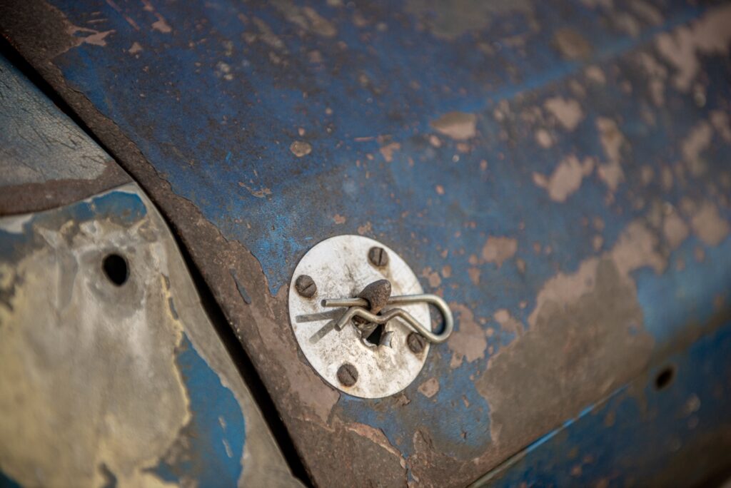 Close-up detail of hood pin mounted on worn blue paint