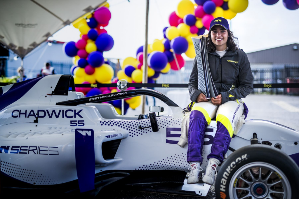 Jamie Chadwick sitting on her W Series car holding a championship trophy