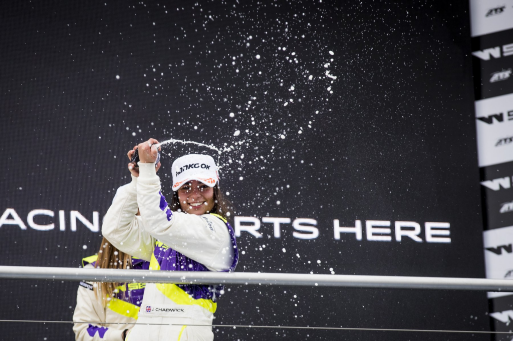 Jamie Chadwick sitting on her W Series car holding a championship trophy