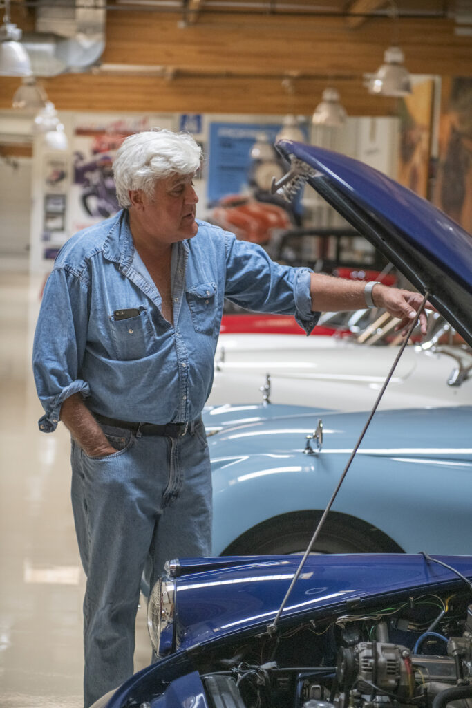 Jay Leno beside blue convertible in his garage