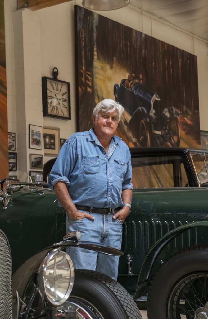Jay Leno beside green brass era car