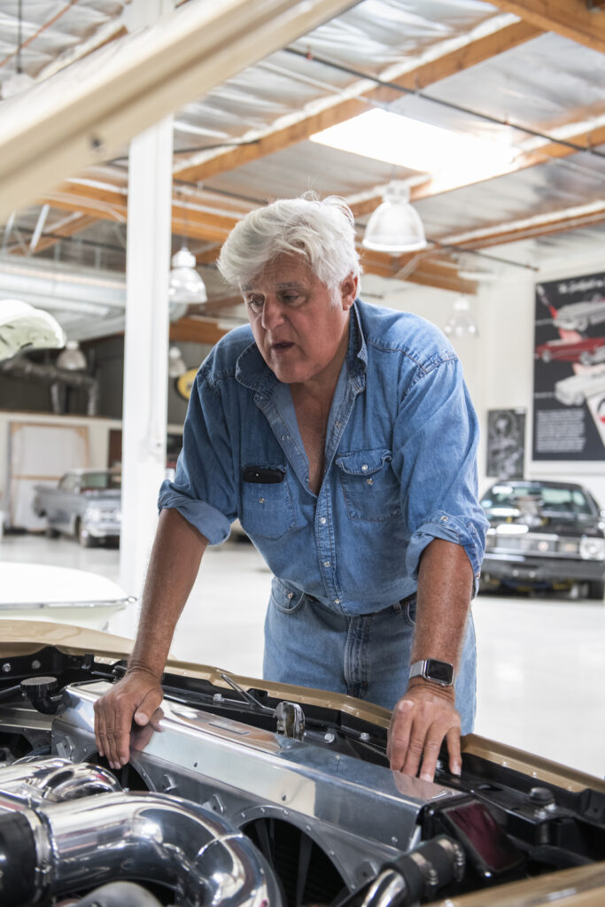 Jay Leno leaning over classic car engine bay