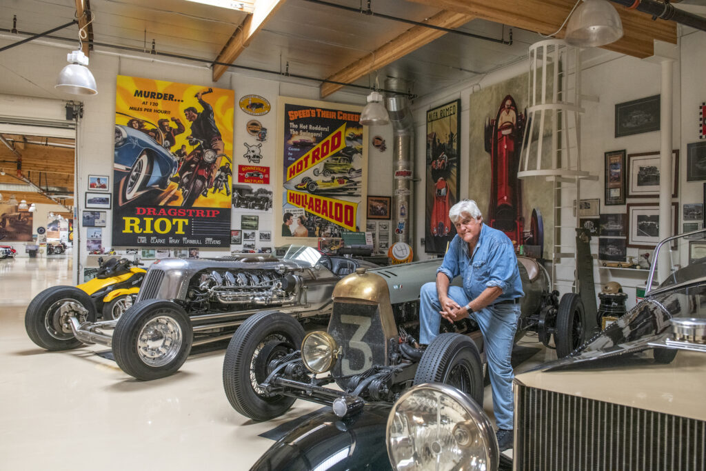 Jay Leno sitting with vintage cars