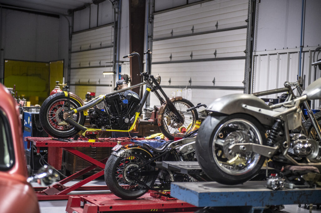 Custom motorcycles on service lifts inside Jesse James’ fabrication workshop.