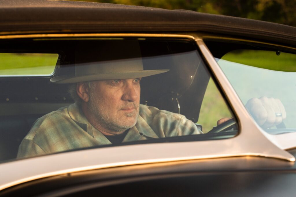 Jesse James driving classic hot rod seen through side window