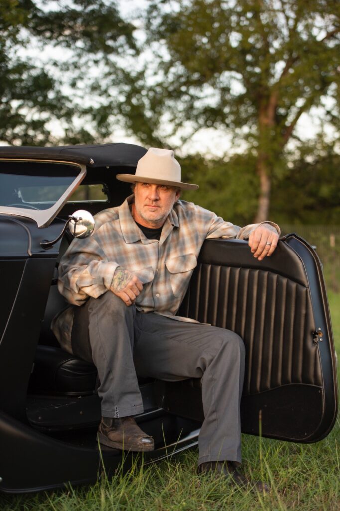 Jesse James sitting in open door of vintage hot rod pickup
