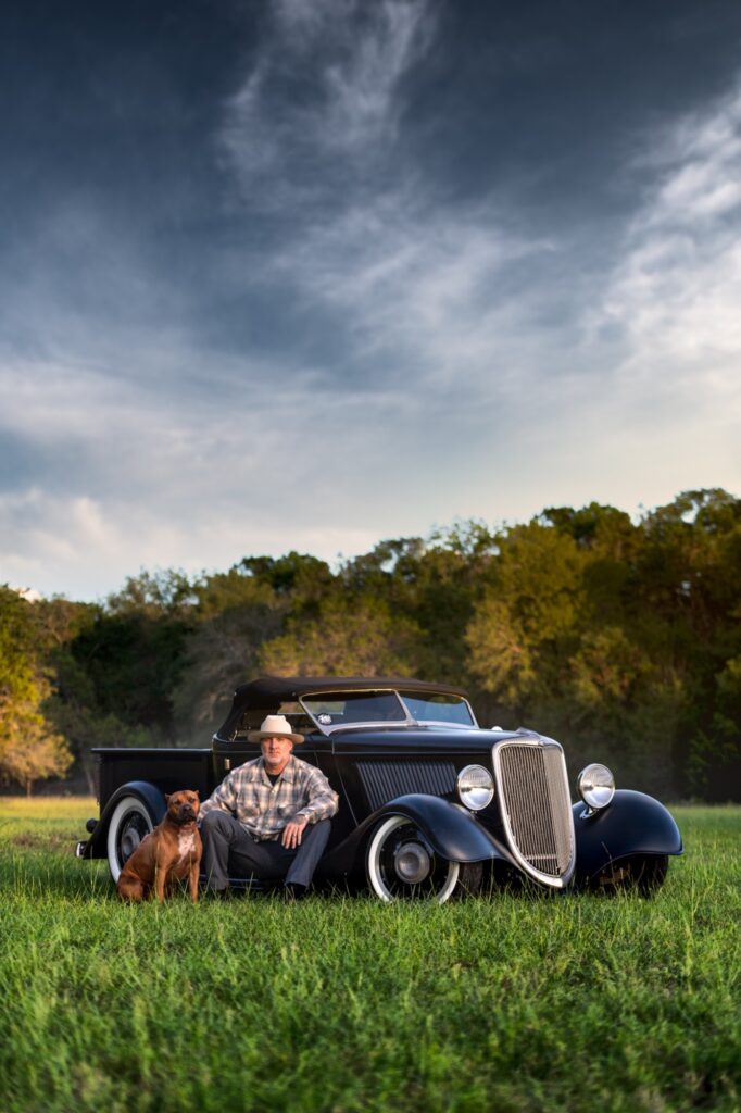 Jesse James and dog beside vintage hot rod pickup in Texas field