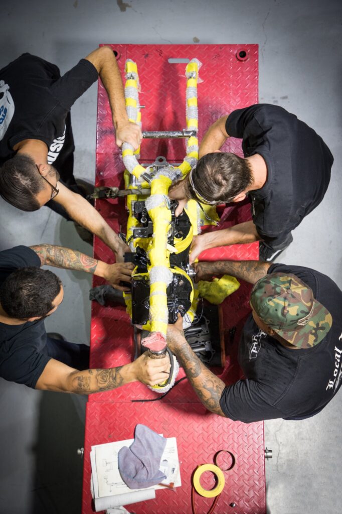Fabrication team assembling motorcycle engine viewed from overhead