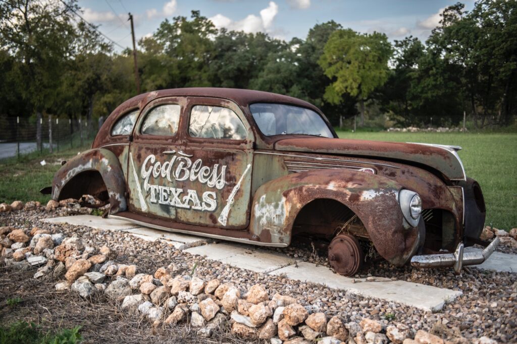Abandoned rusty vintage car with “God Bless Texas” lettering
