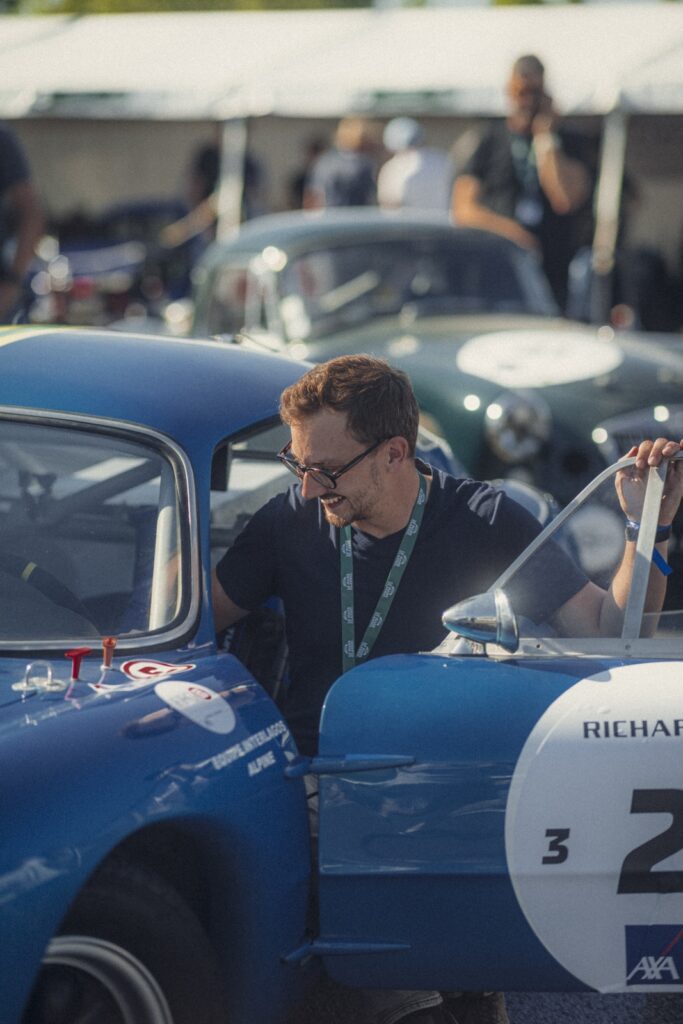 Man opening the door of a blue vintage race car in the paddock