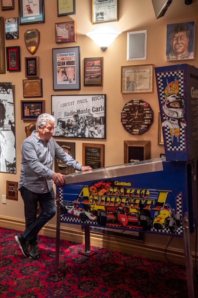 Mario Andretti standing with a vintage pinball machine