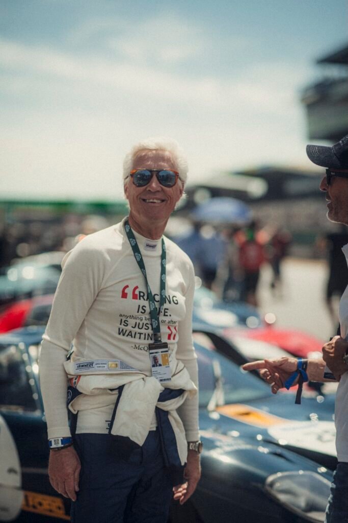 Smiling man wearing sunglasses and racing shirt standing in the paddock during Le Mans Classic