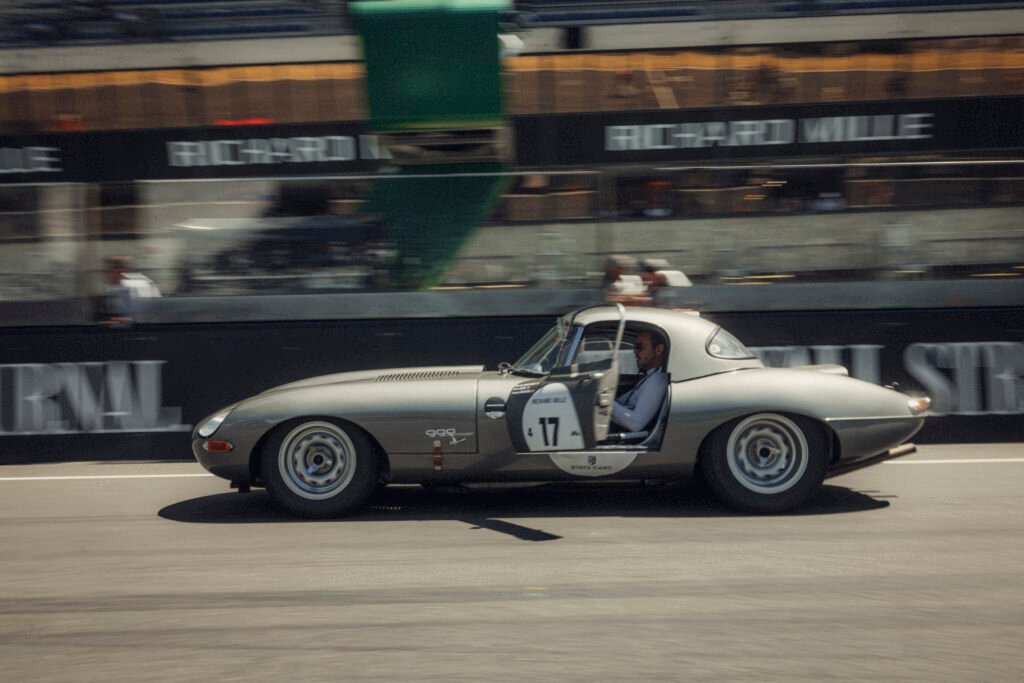 Silver vintage coupe race car driving along the circuit past grandstands at Le Mans Classic, organised by Peter Auto