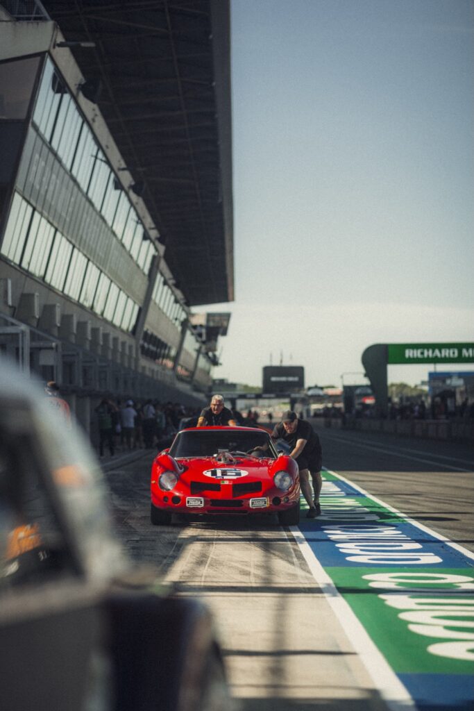 Red vintage race car being pushed along pit lane at Classic Le Mans
