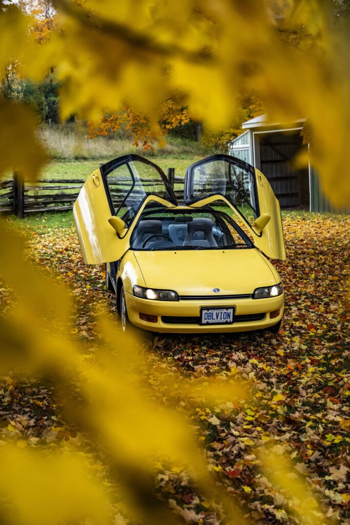 Yellow Toyota Sera front view with butterfly doors open among leaves