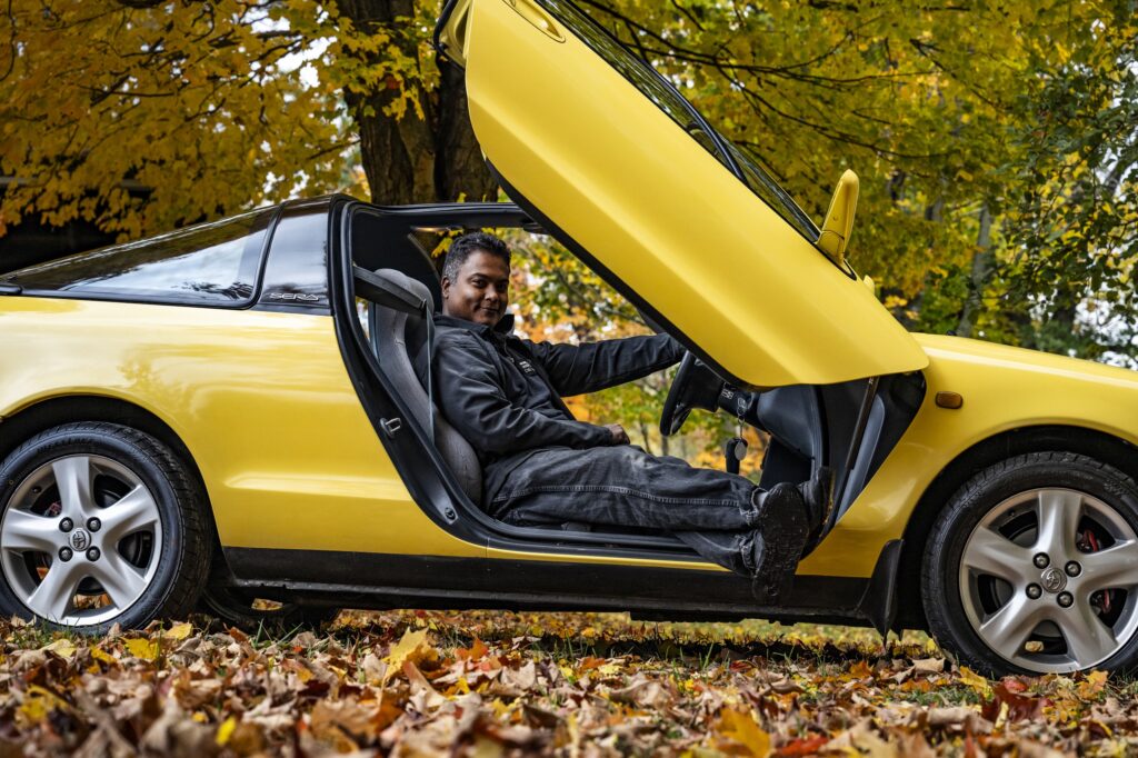 Driver seated in yellow Toyota Sera with butterfly door raised