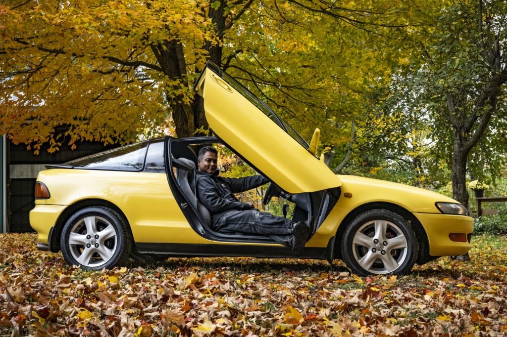 Driver seated in yellow Toyota Sera side profile with door open