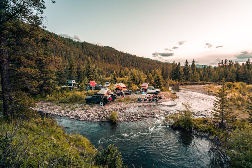 Overland vehicles camped beside a river in a forest clearing