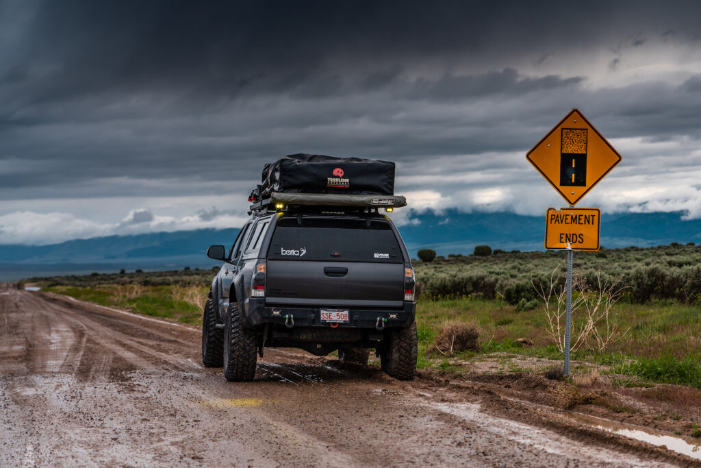 Toyota Tacoma overland build parked at a pavement ends sign on a dirt road under stormy skies