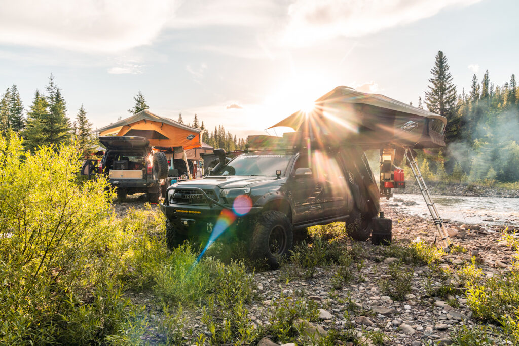 Toyota Tacoma rooftop tent setup beside a river with sun flare
