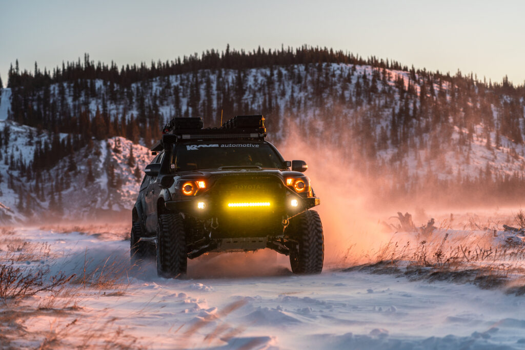 Toyota Tacoma driving through snow at sunset with lights on
