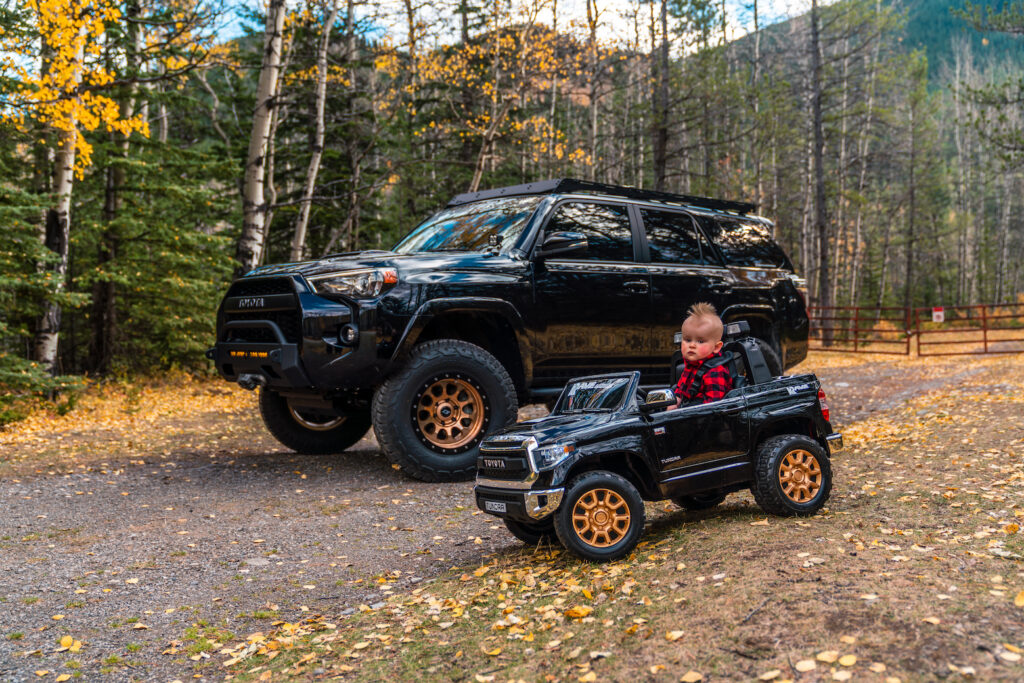 Toyota 4Runner parked beside a child driving a toy truck in a forest setting
