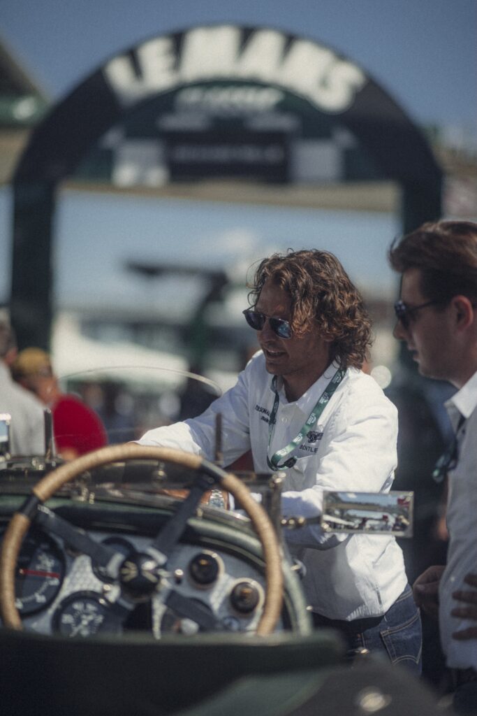 Orange classic Porsche parked beneath a floral archway at a motorsport event