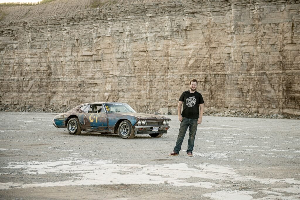 Man standing beside vintage Chevrolet Chevelle race car in gravel quarry